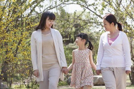 Multi-generational family, grandmother, mother, and daughter holding hands and going for a walk in the park in springtimeの写真素材
