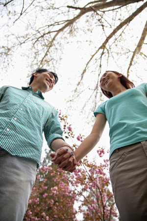 Happy smiling young couple holding hands in the park in springtime, low angle viewの写真素材