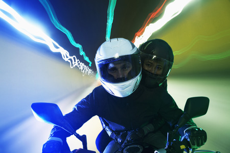 Young couple riding a motorcycle through the city streets at night in Beijing, light trails