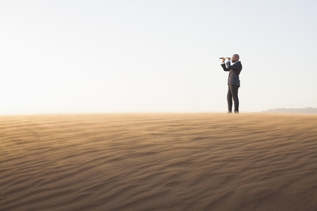 Young businessman looking through telescope in  the middle of the desertの写真素材