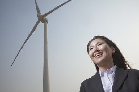 Portrait of smiling young businesswoman standing by a wind turbineの写真素材