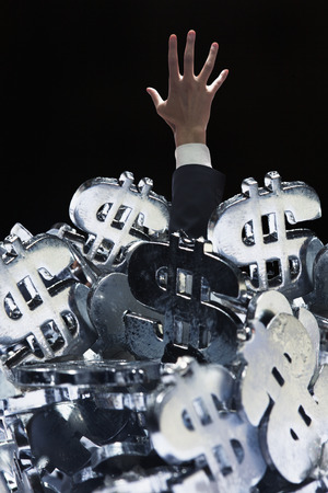 Businessman buried under a large group of dollar signs, trying to get outの写真素材