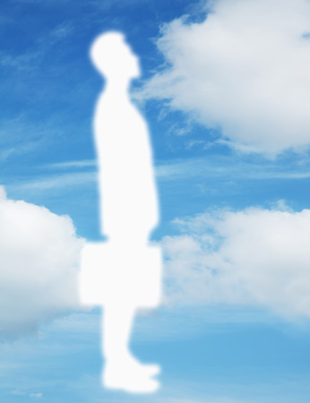 Silhouette of businessman holding a briefcase with a blue sky and clouds behind himの写真素材