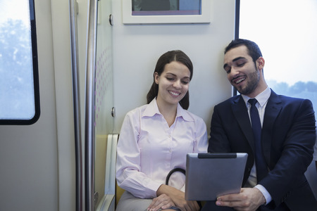 Two young business people sitting and looking at a digital tablet on the subwayの写真素材