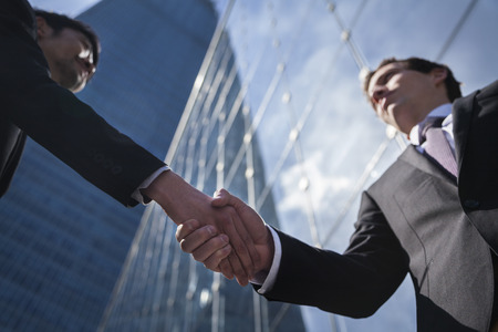 Two businessmen shaking hands in Beijing, China, view from belowの写真素材