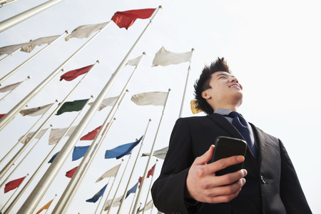 Smiling young businessman holding a phone with flags in the backgroundの写真素材