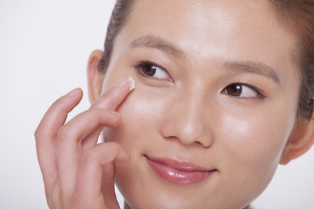 Close up on the face of a smiling young woman applying cream to her face, studio shotの写真素材