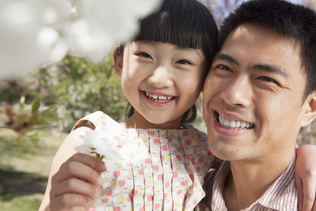 Smiling father and daughter enjoying the cherry blossoms on the tree in the park in springtimeの写真素材