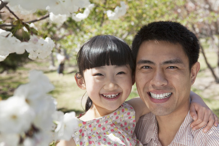 Smiling father and daughter enjoying the cherry blossoms on the tree in the park in springtime, portraitの写真素材