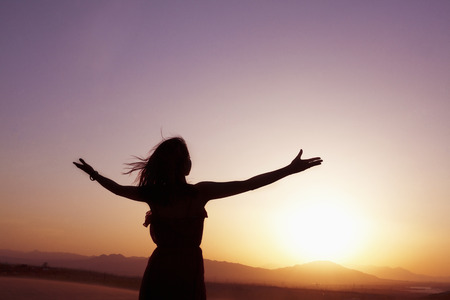 Serene young woman with arms outstretched doing yoga in the desert in China, Silhouetteの写真素材
