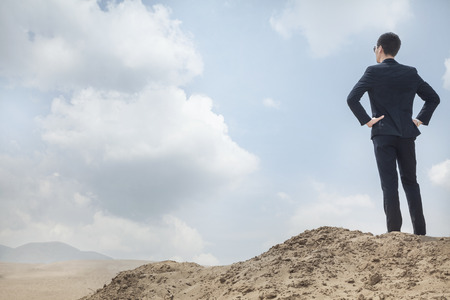 Young businessman standing with hands on hips looking out over the desertの写真素材