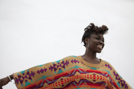Portrait of young smiling woman holding her arms out in traditional clothing from Africa, studio...