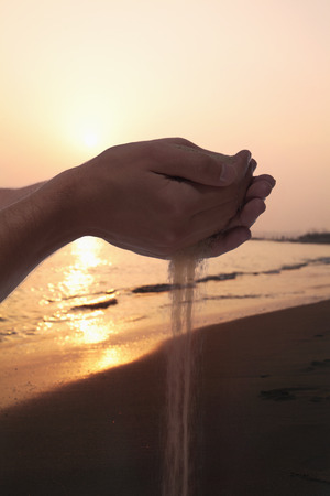 Hands holding and spilling sand with beach at sunset in the backgroundの写真素材