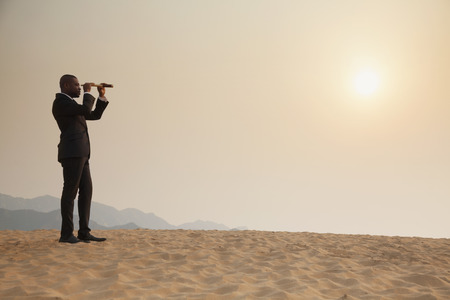 Young businessman looking through telescope in  the middle of the desertの写真素材