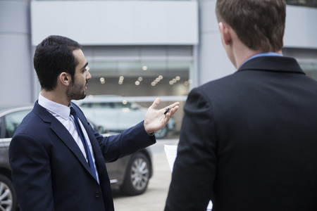 Car salesman holding car keys and selling a car to a young businessmanの写真素材