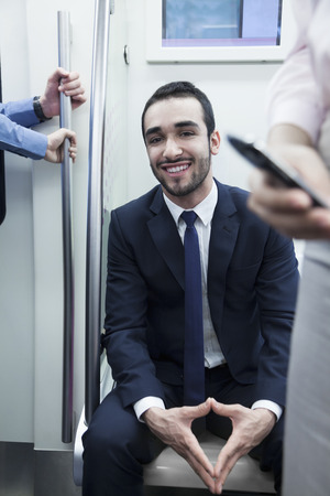 Portrait of young smiling businessman sitting on the subway and looking at cameraの写真素材