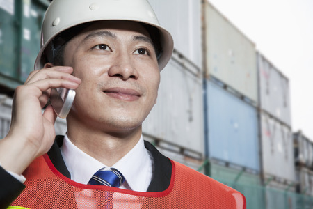 Smiling engineer in protective workwear on the phone in a shipping yardの写真素材