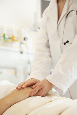 Close up of doctor holding a patients hands lying down on a hospital bedの写真素材