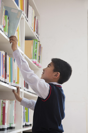 Schoolboy reaching for book off bookshelfの写真素材