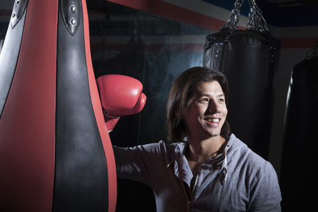 Portrait of smiling young man at the boxing gym leaning on punching bagの写真素材