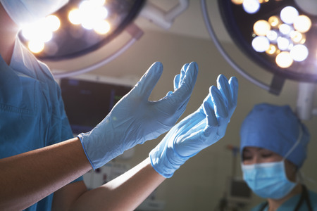 Midsection view of hands in surgical gloves and surgical lights in the operating room の写真素材