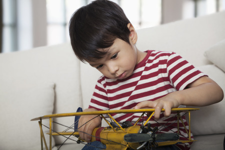 Little boy looking down and holding a model airplane,  on the couch in the living roomの写真素材