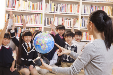 Teacher teaching geography to schoolchildren with a globeの写真素材