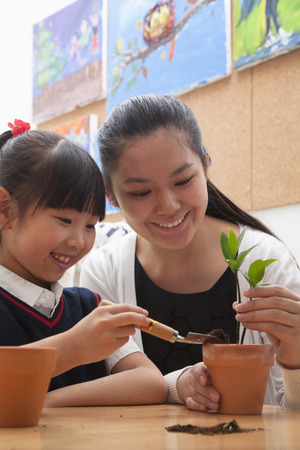 Teacher and schoolgirl planting plants into flowerpotsの写真素材