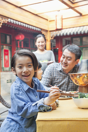 Portrait of little girl eating dinner with her familyの写真素材