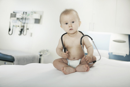 Portrait of baby sitting on an examination table in the doctors office with a stethoscope around his neckの写真素材