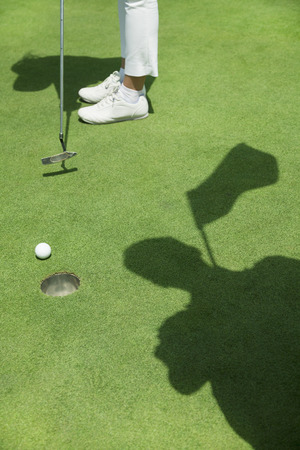 Low section of young woman hitting the ball on the golf course, focus on the holeの写真素材