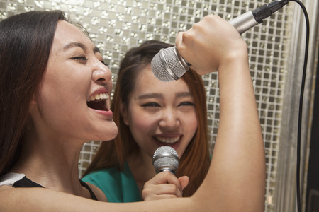 Two young female friends singing into a microphone at karaokeの写真素材