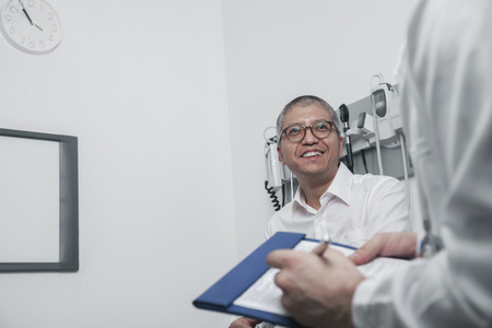 Doctor writing on medical chart with a smiling patientの写真素材