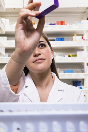 Pharmacist taking down and examining prescription medication in a pharmacyの写真素材