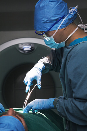 Surgeon looking down, working, and holding surgical equipment with patient lying on the operating tableの写真素材