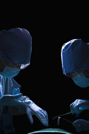Two surgeons looking down, working, and holding surgical equipment with patient lying on the operating table の写真素材