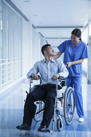 Smiling female nurse pushing and assisting patient in a wheelchair in the hospital の写真素材