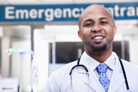 Portrait of smiling doctor outside of the hospital, emergency room sign in the backgroundの写真素材