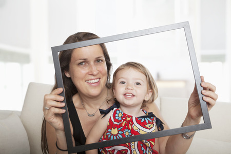 Mother and daughter holding up a picture frame and looking through itの写真素材