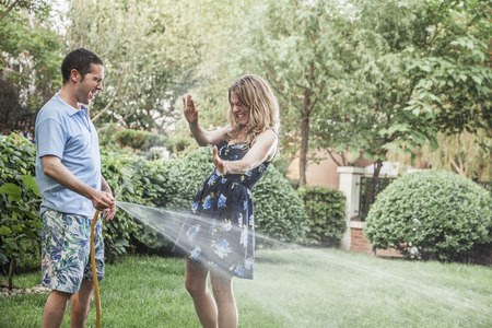 Couple playing with a garden hose and spraying each other outside in the garden  の写真素材