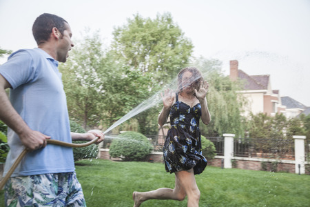 Couple playing with a garden hose and spraying each other outside in the garden の写真素材