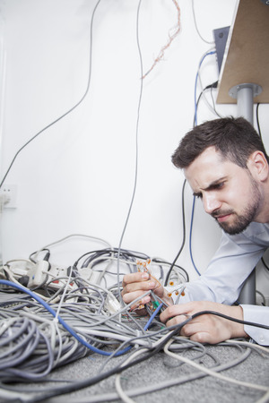 Frustrated man lying down trying to figure out and sort  computer cablesの写真素材