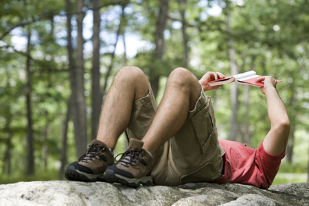 Man lying on a rock reading a bookの写真素材