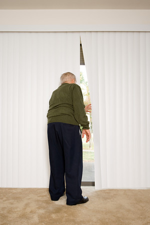 Elderly man looking out of blindsの写真素材