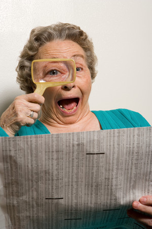 Woman reading newspaper with magnifying glassの写真素材