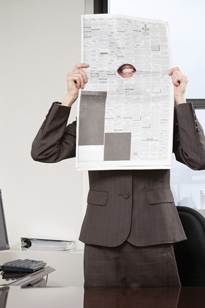 Woman smiling through hole in newspaperの写真素材