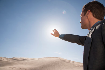 Businessman framing sun through fingers in desertの写真素材