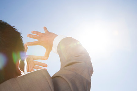 Businessman framing sun through fingers in desertの写真素材