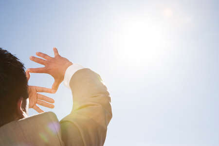 Businessman framing sun through fingers in desertの写真素材