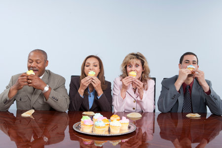 Business colleagues eating cupcakes in officeの写真素材